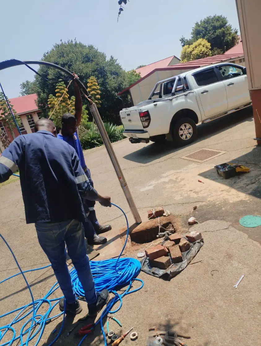 Two workers installaing a borehole pump
